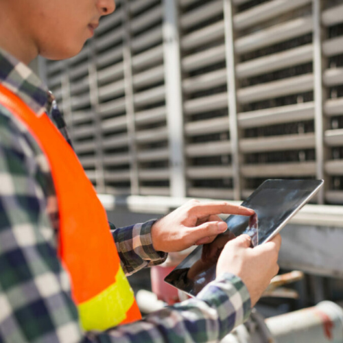 Industrial field technician using a mobile app on a tablet for equipment inspection.